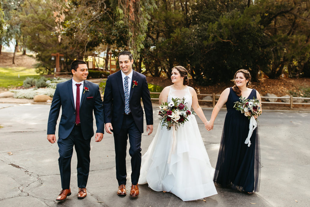 bride hold bridesmaids hand while taking photos with groom and groomsman
