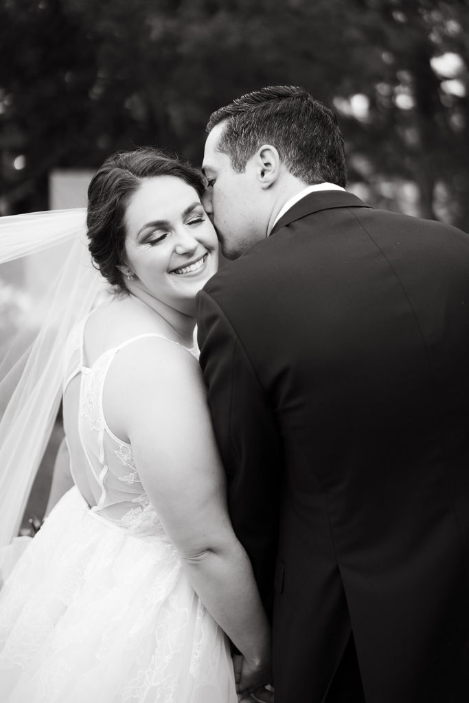 groom kisses bride's cheek in black and white wedding photo