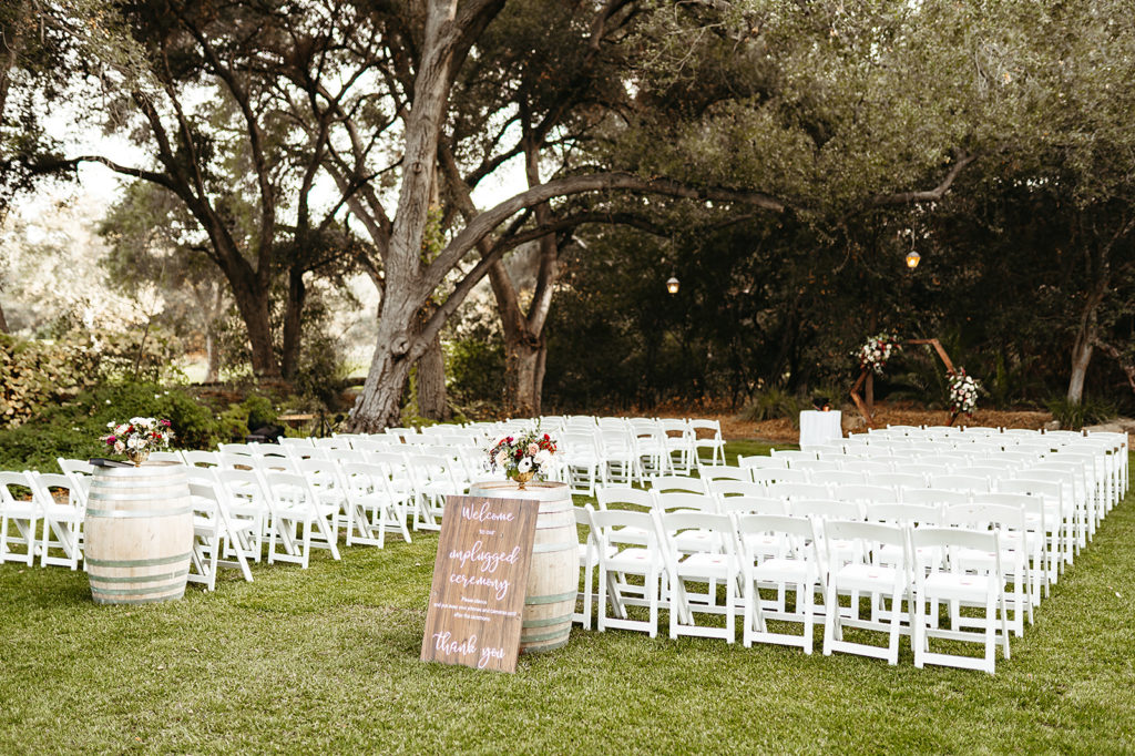 hygge wedding ceremony at Temecula Creek Inn with white chairs and wooden geometric ceremony arch and sign for unplugged ceremony