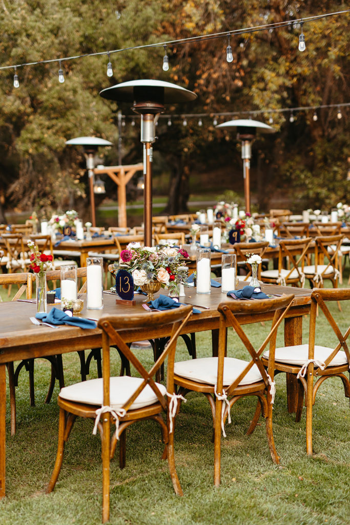 wedding reception at Temecula Creek Inn with wooden farmhouse tables, chairs and blue napkins with dark blue table numbers