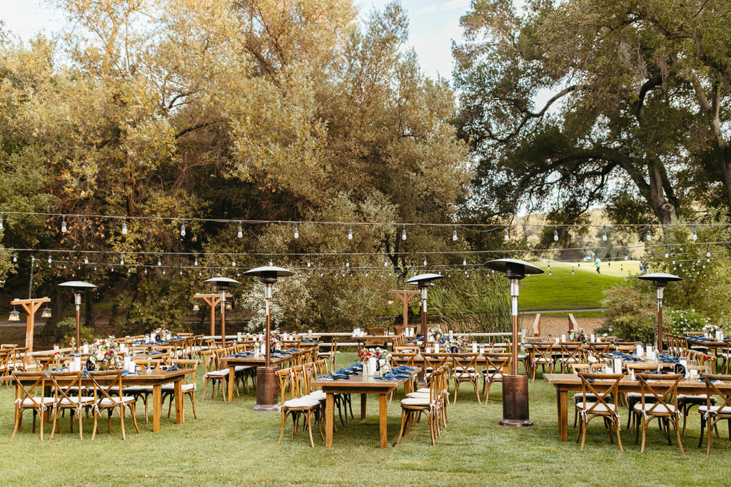 wedding reception at Temecula Creek Inn with wooden farmhouse tables, chairs and blue napkins with dark blue table numbers