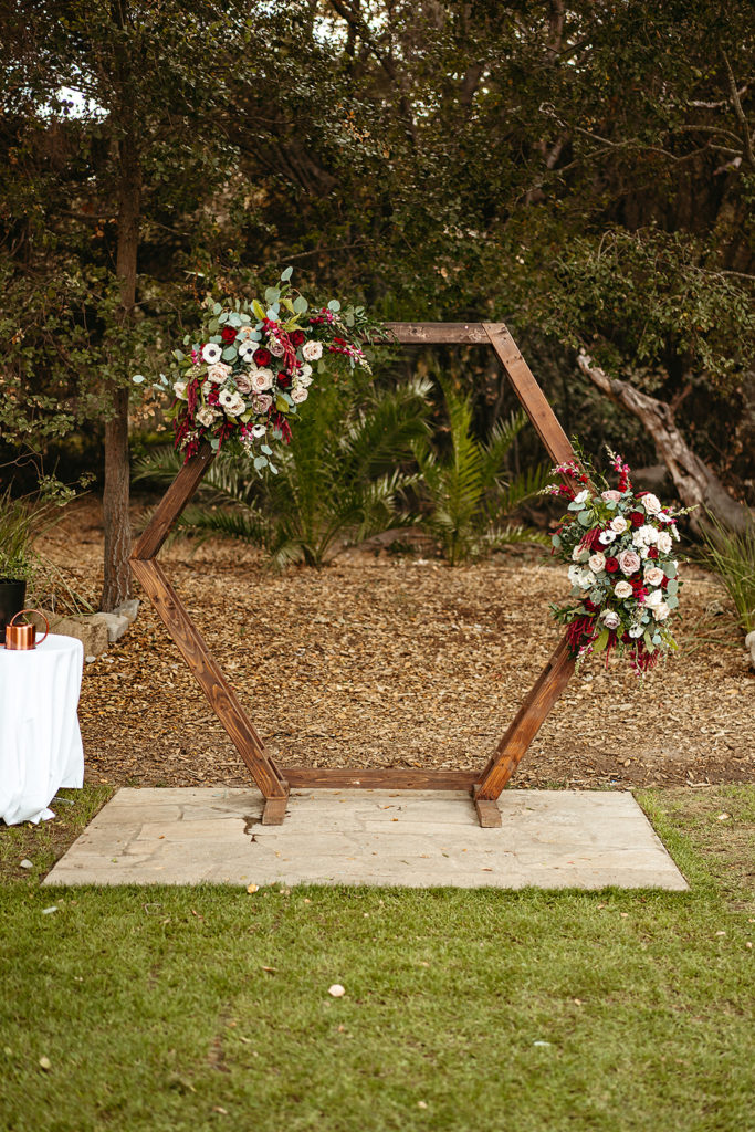 wooden geometric ceremony arch with red, white, blue and green floral accents