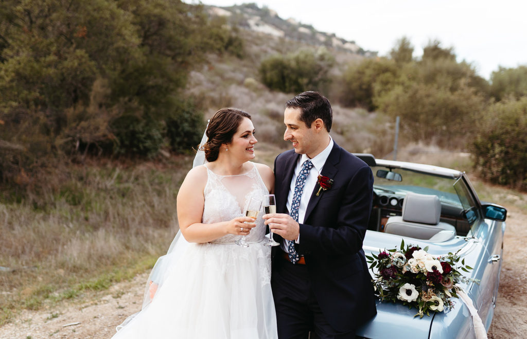 bride and groom cheers with champagne while sitting on vintage blue Mercedes 