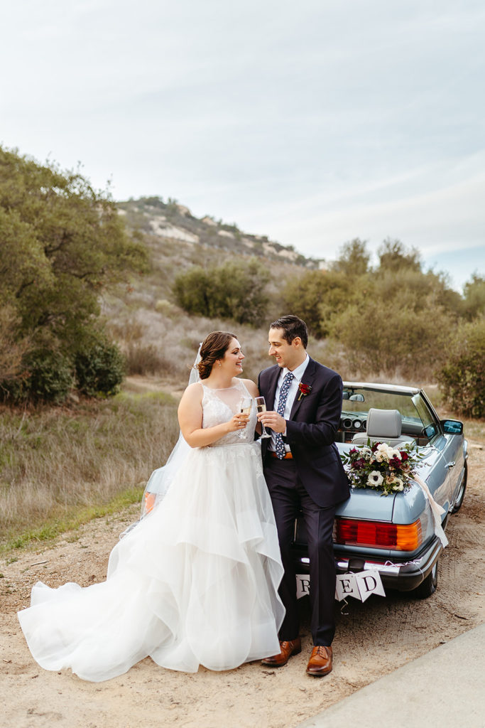 bride and groom cheers with champagne while sitting on vintage blue Mercedes get away car
