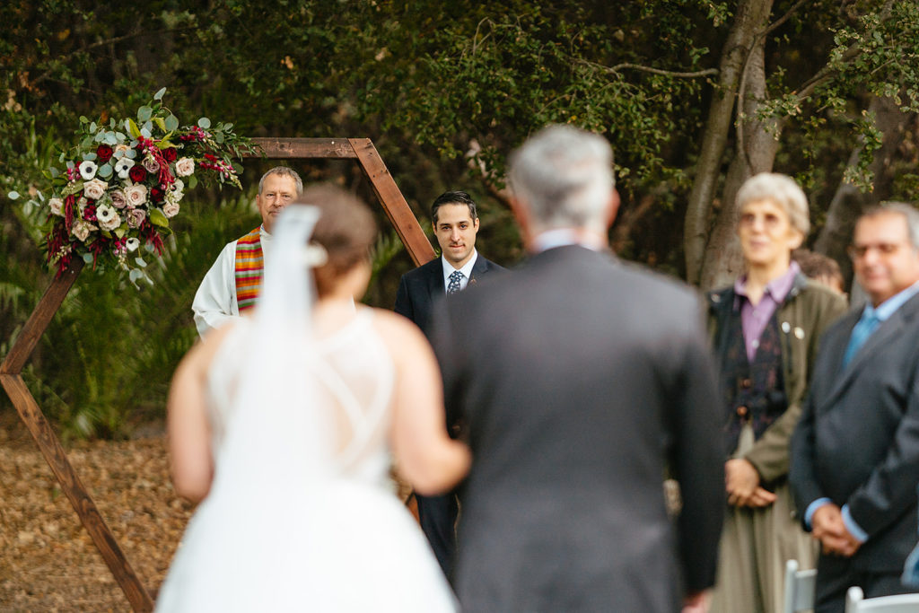 groom at the end of the aisle as bride walks towards him