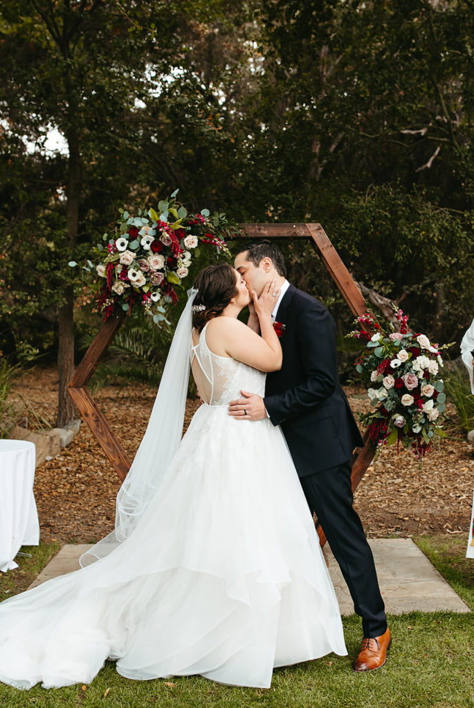 bride and groom first kiss with wooden geometric wedding arch behind them