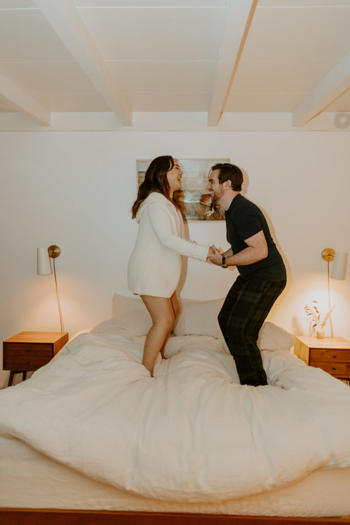 engaged couple jumping on bed during engagement photo session in Palm Springs