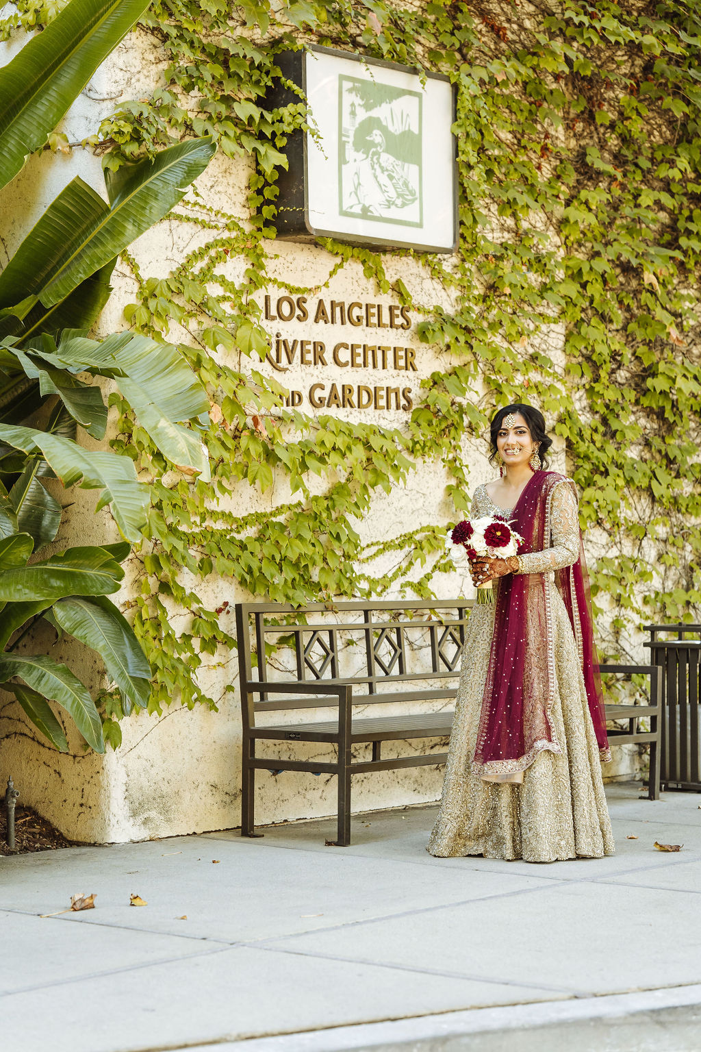 bride wearing embellished golden wedding saree holds bridal bouquet with white and maroon flowers