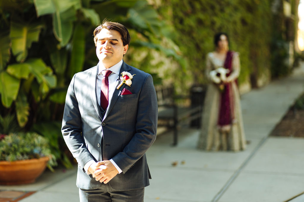 bride wearing embellished golden wedding saree and groom in dark grey suit with maroon tie does a first look at Los Angeles River and Garden Center