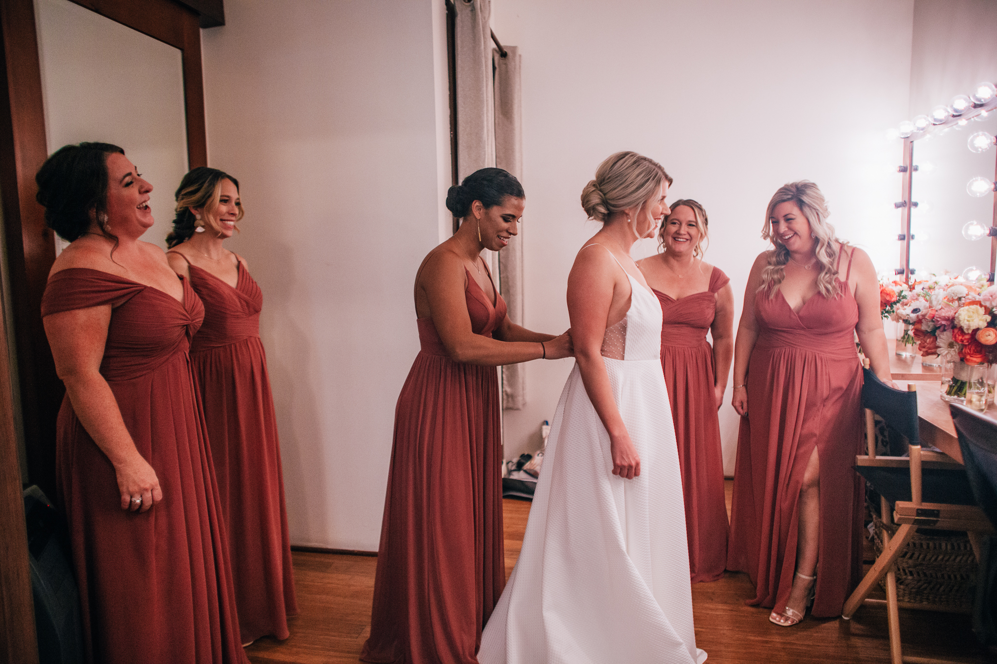 bride getting into her wedding dress with bridesmaids in mauve dresses 