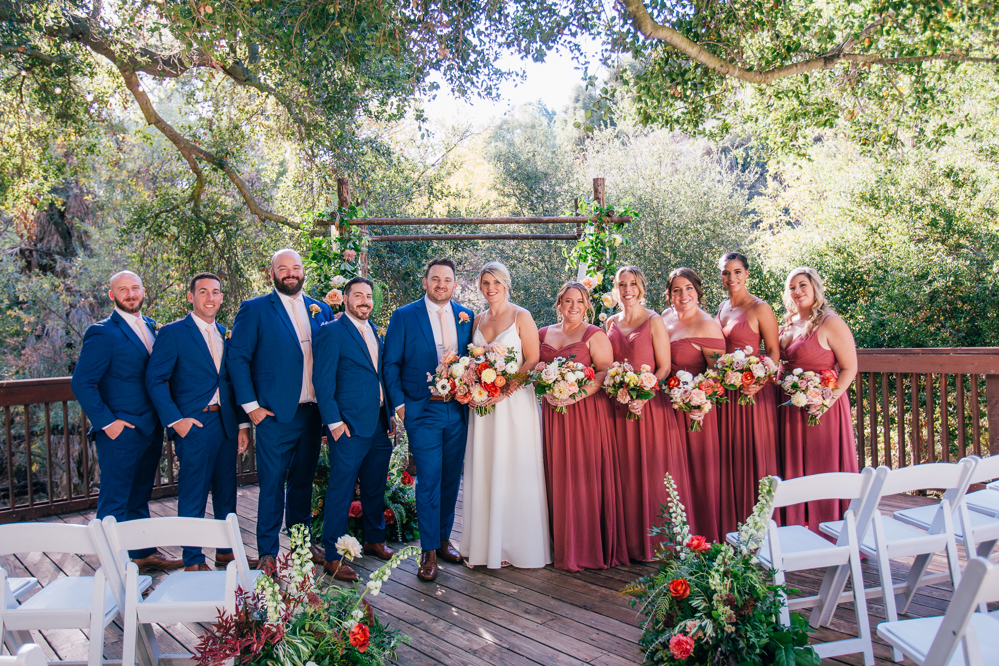 bride and groom stand with their wedding party in blue suits and mauve dresses