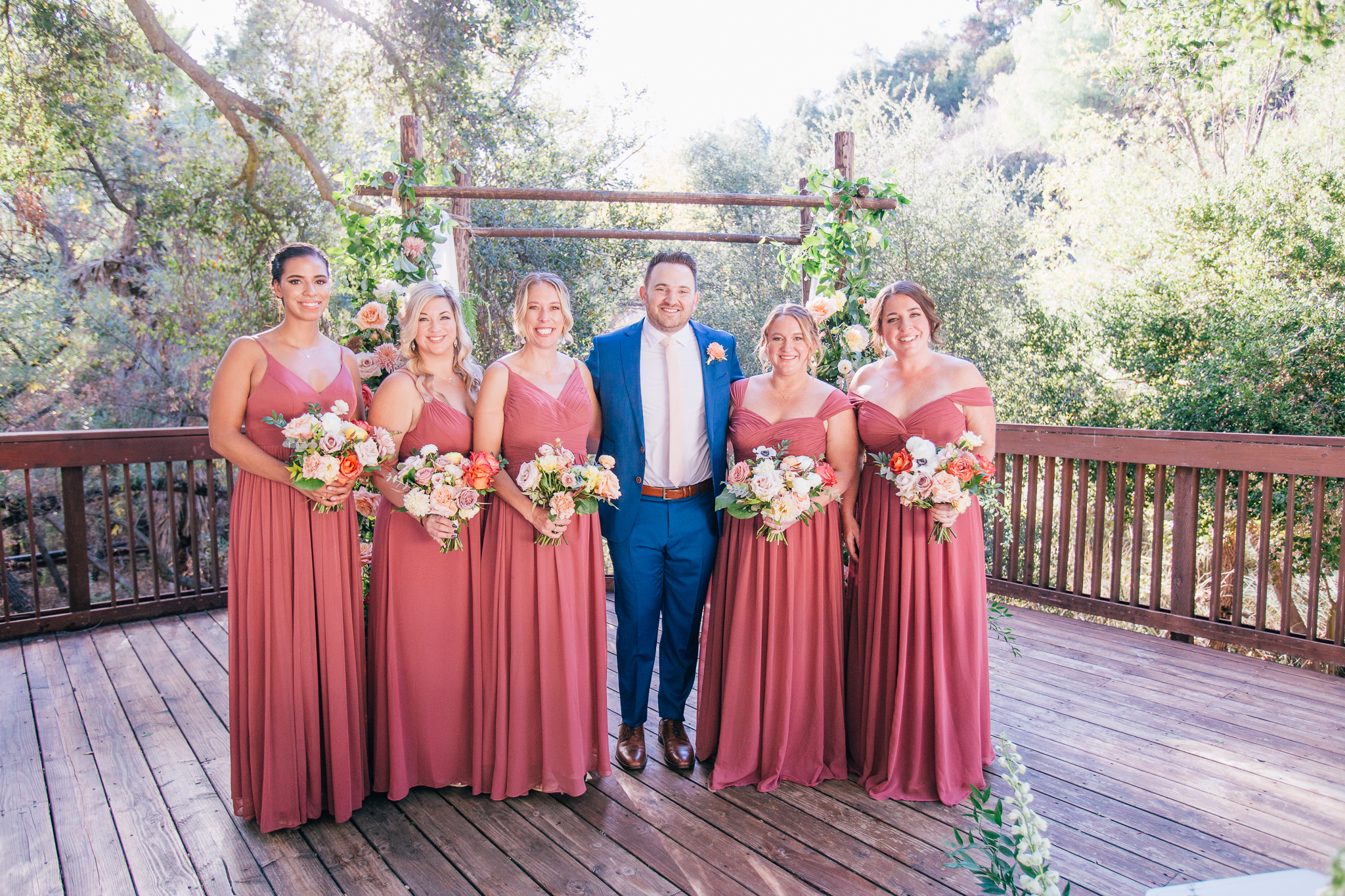 groom in blue suit stands with bridesmaids in mauve dresses