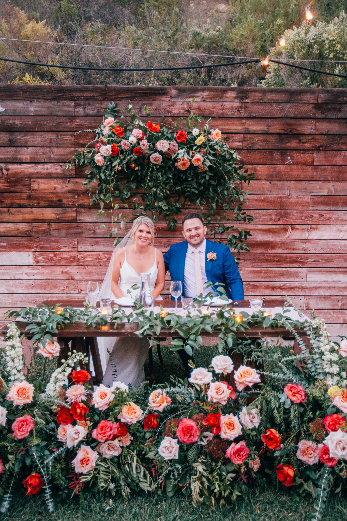 bride and groom at sweetheart table surrounded by bright and colorful florals