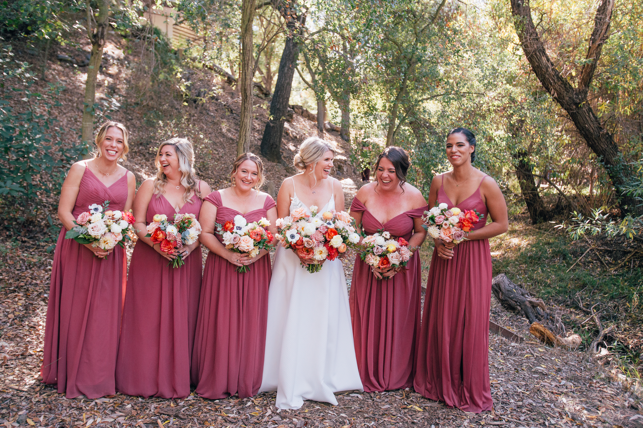 bride stands with bridesmaids in mauve dresses while holding bright and vibrant wedding bouquets