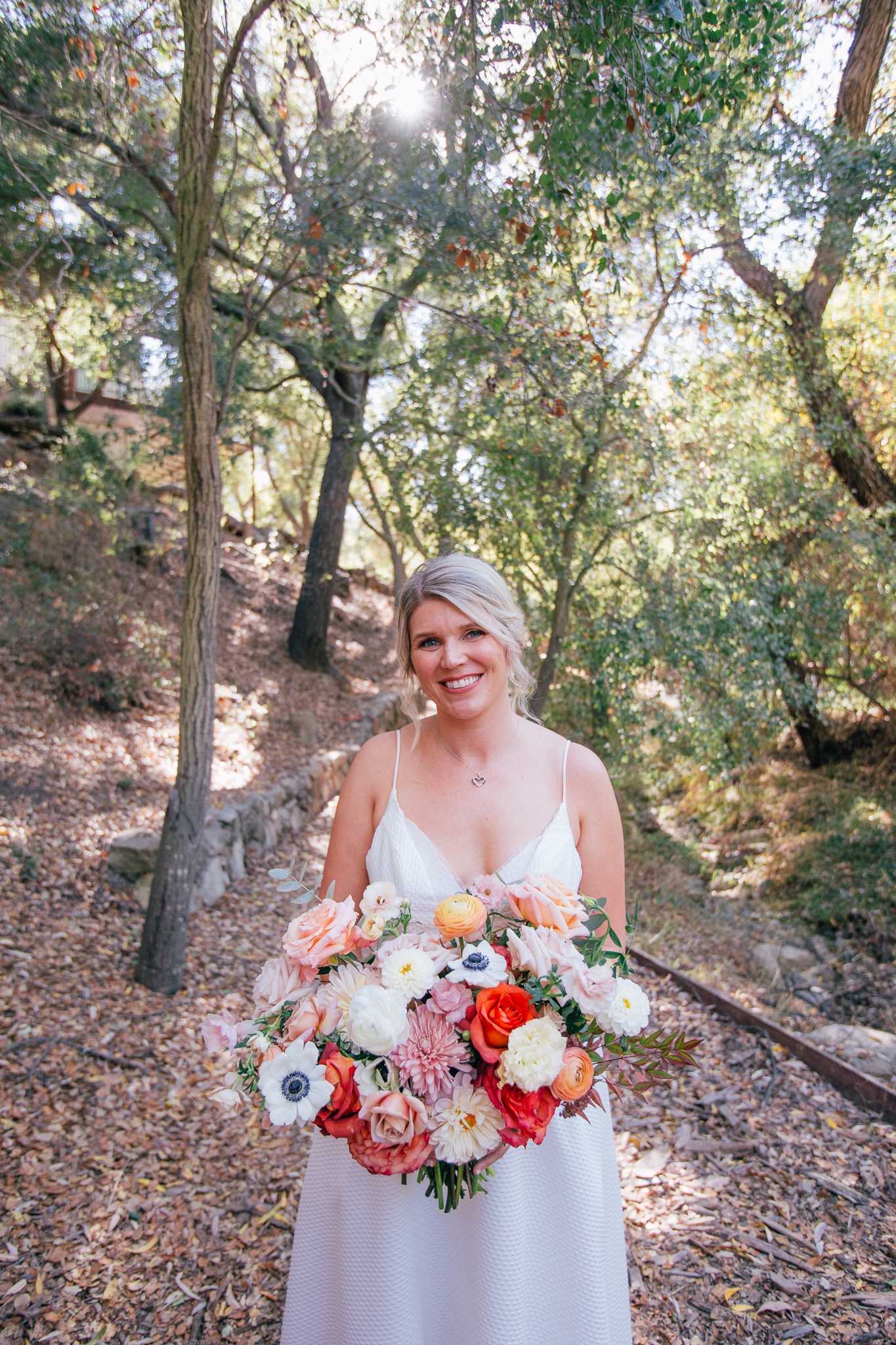 bride in spaghetti strap dress stands with bright and vibrant wedding bouquet with mixture of colorful flowers