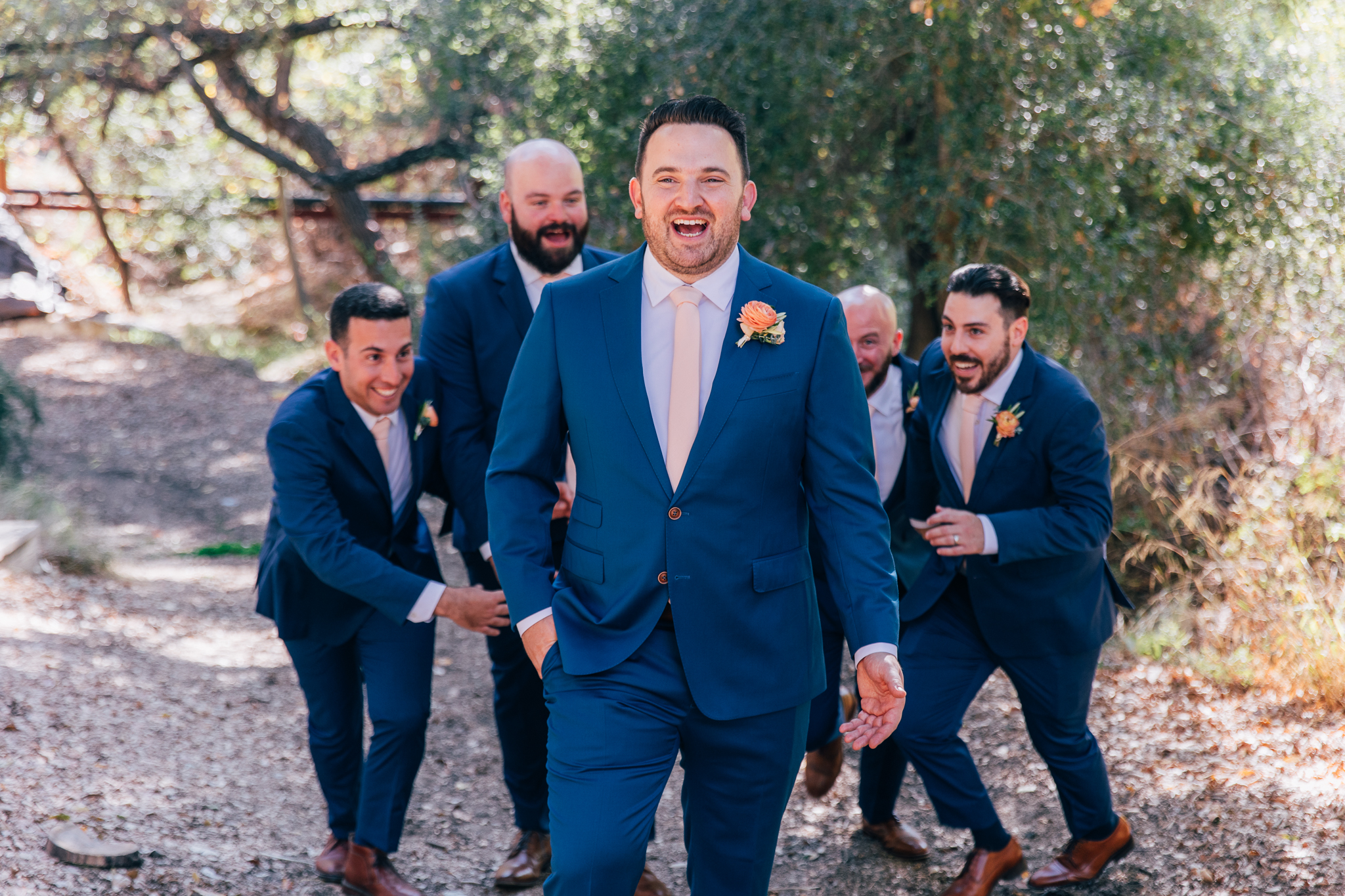 groom stands with groomsmen in blue suits with light pink ties and brown shoes