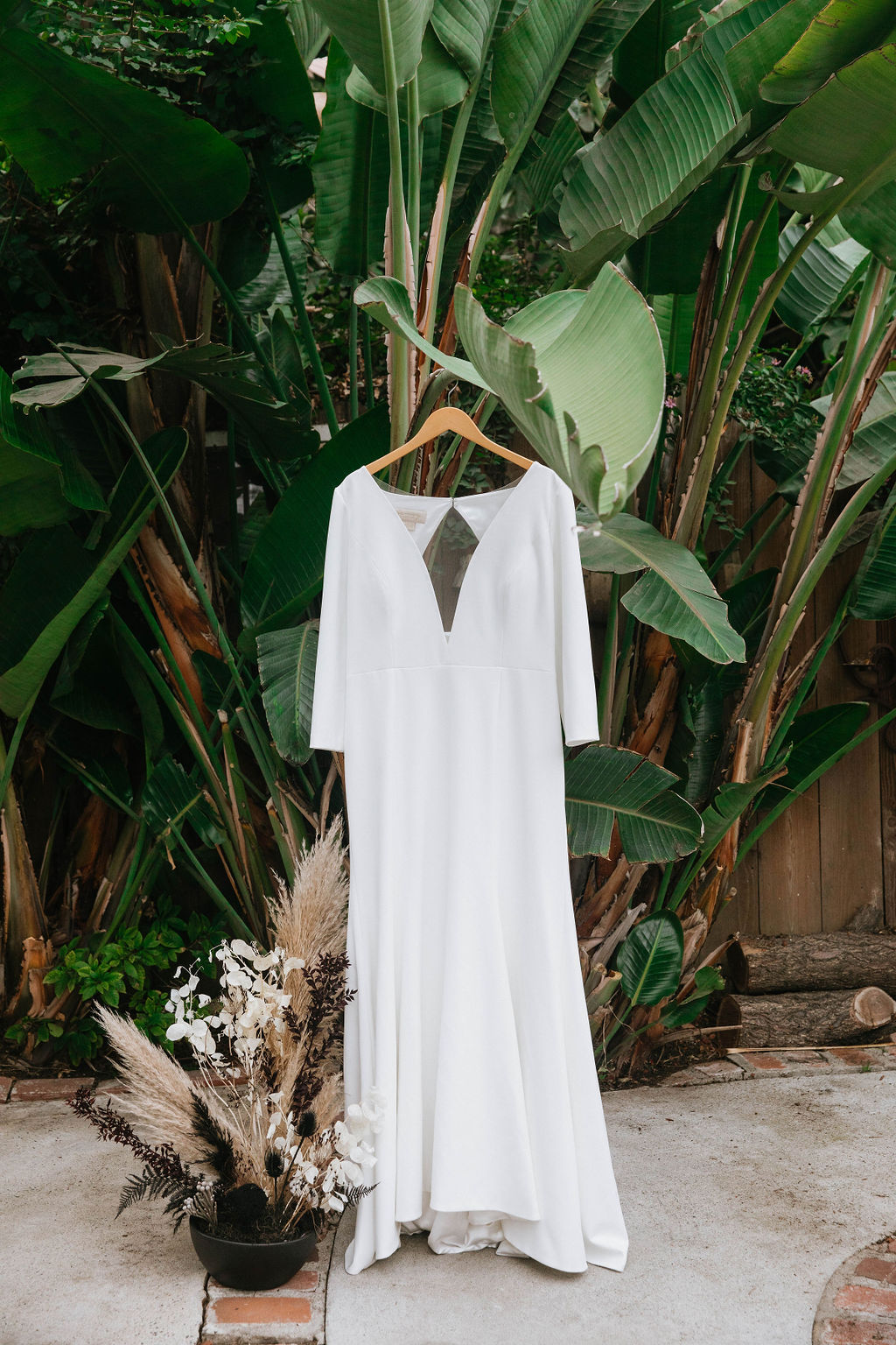 long sleeve deep vneck wedding dress hanging next to planter of dried florals