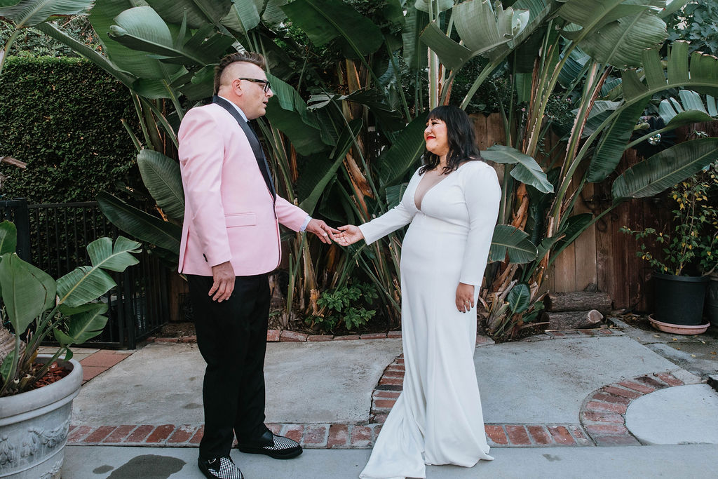 bride in long sleeve deep v-neck wedding dress has first look with groom in pink suit jacket and houndstooth shoes 