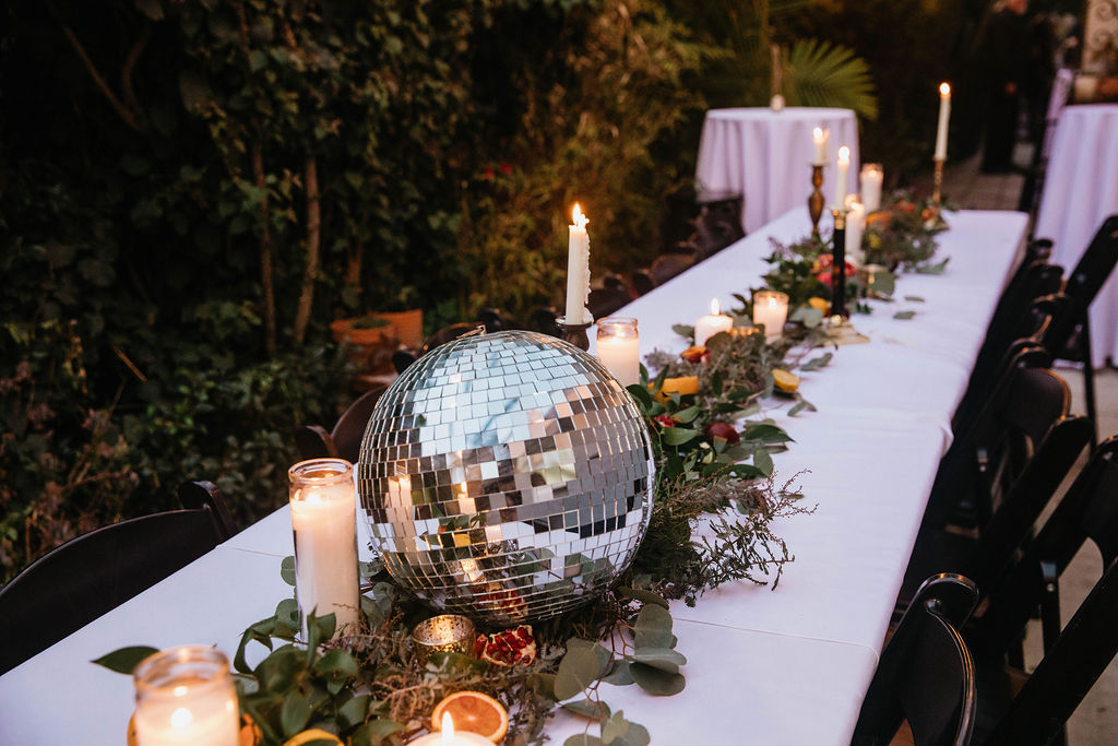 backyard wedding reception with long table draped in dried florals, fruit, candles and a disco ball 