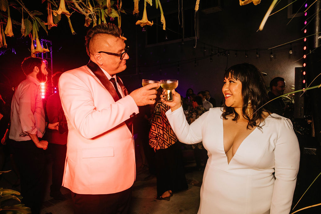 bride in long sleeve deep v-neck wedding dress cheers groom in pink suit jacket 