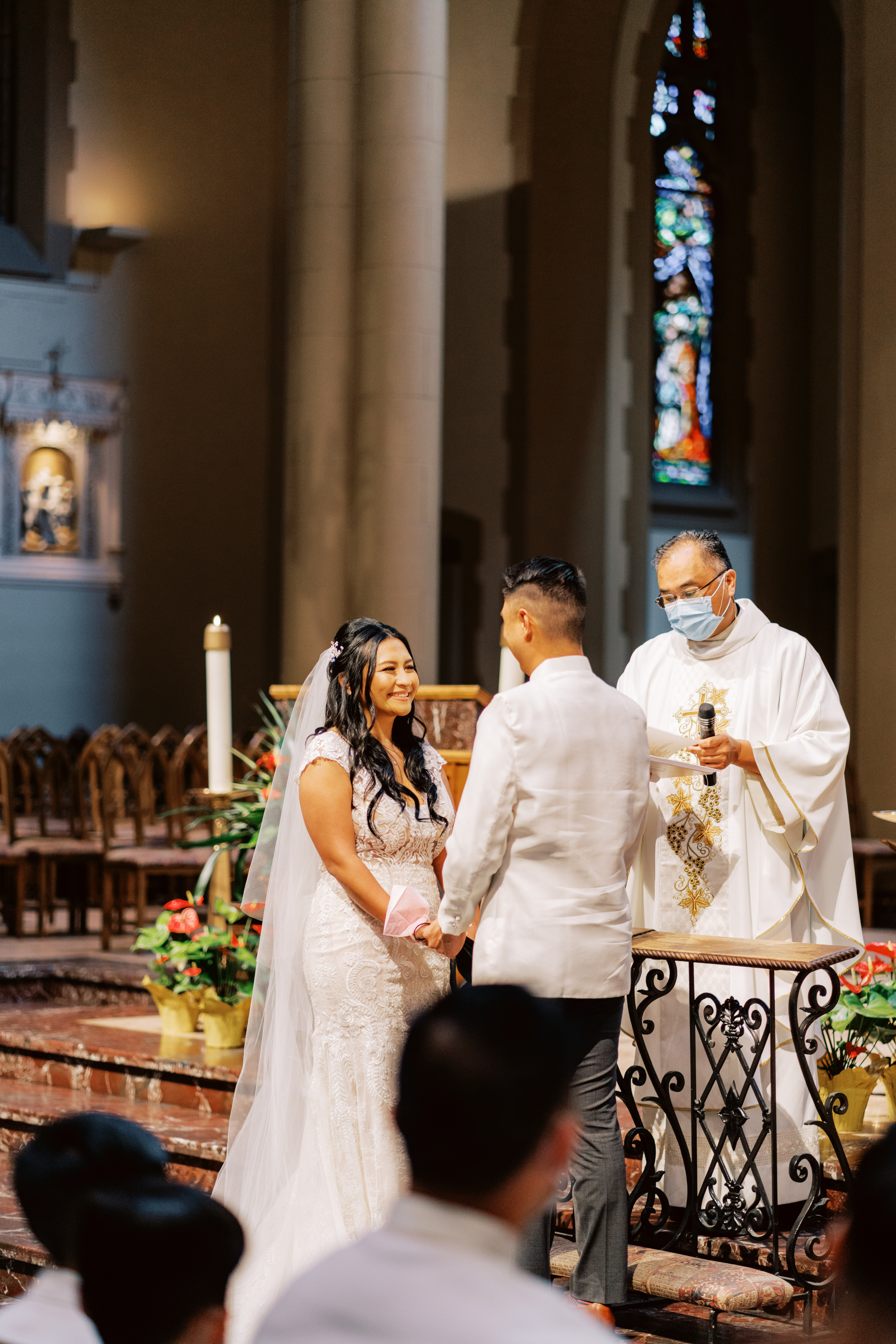 smiling bride and groom hold hands at the altar during Catholic Church wedding ceremony