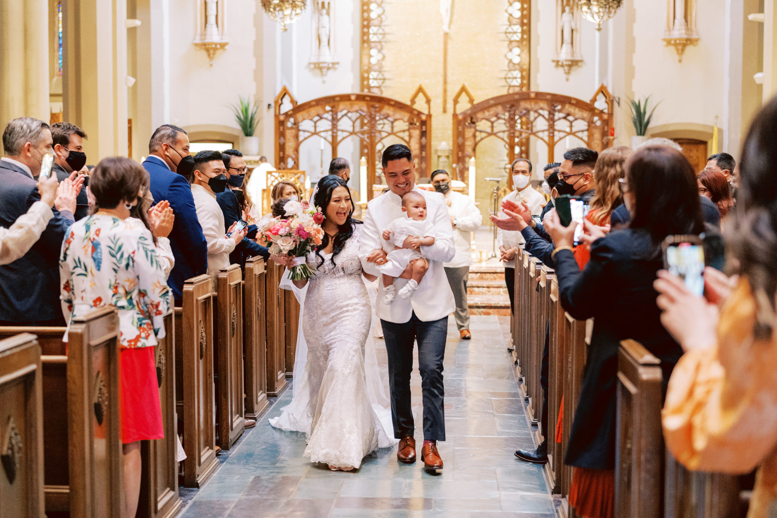 bride and groom hold their baby during their postponed wedding ceremony while walking down the altar
