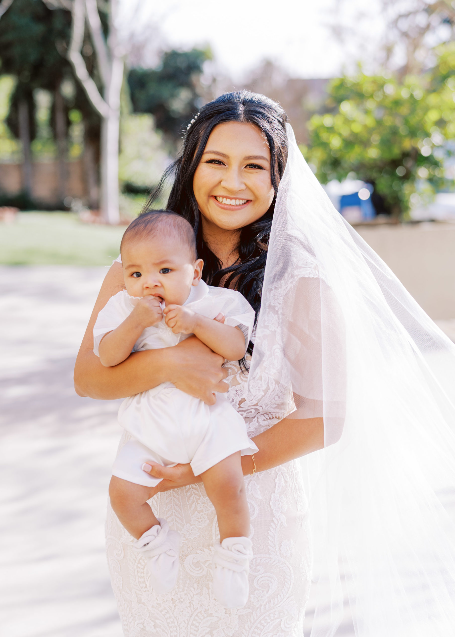 bride in lace wedding dress holds baby during wedding portrait shots