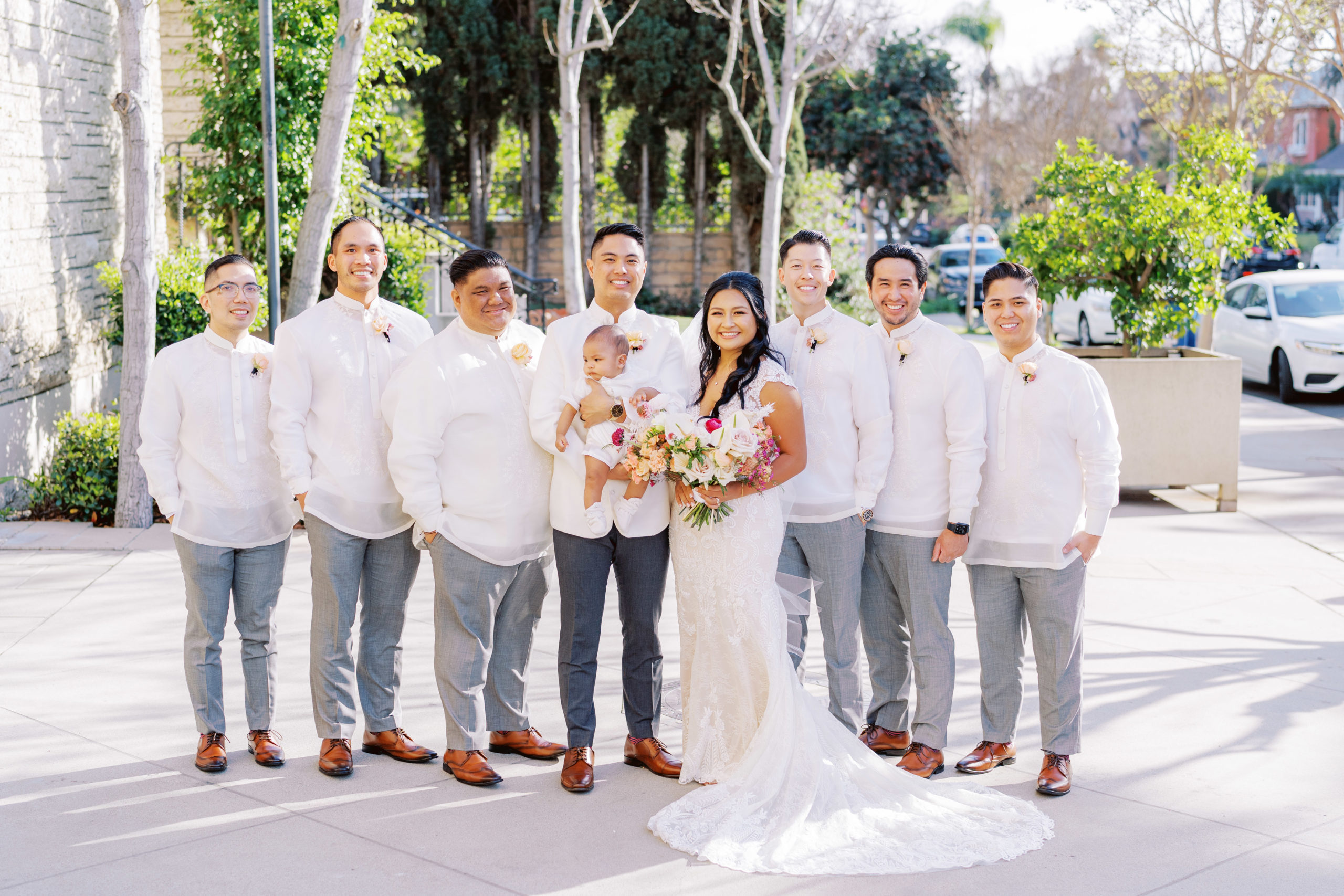 bride and groom stand with groomsmen in white traditional wedding attire