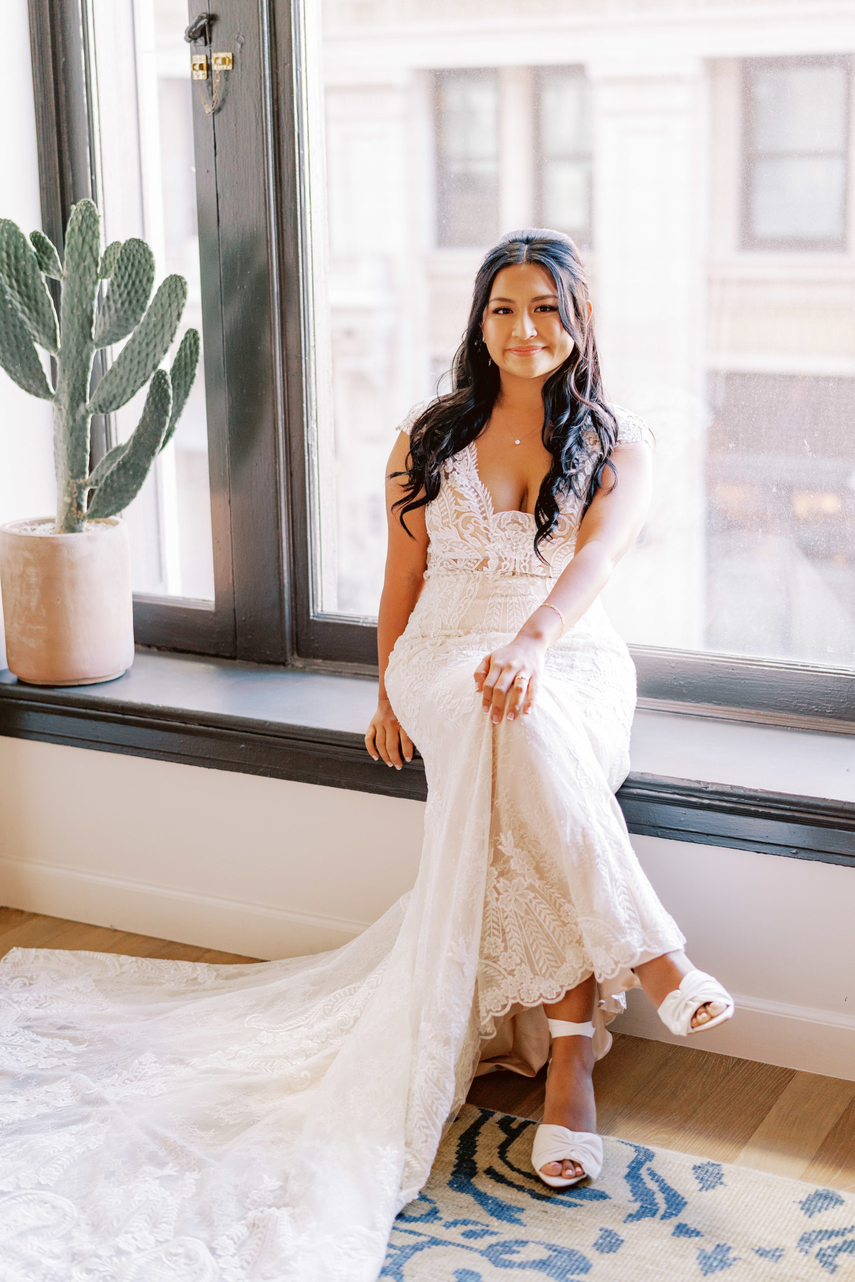 bride in lace wedding dress sits on window for photo