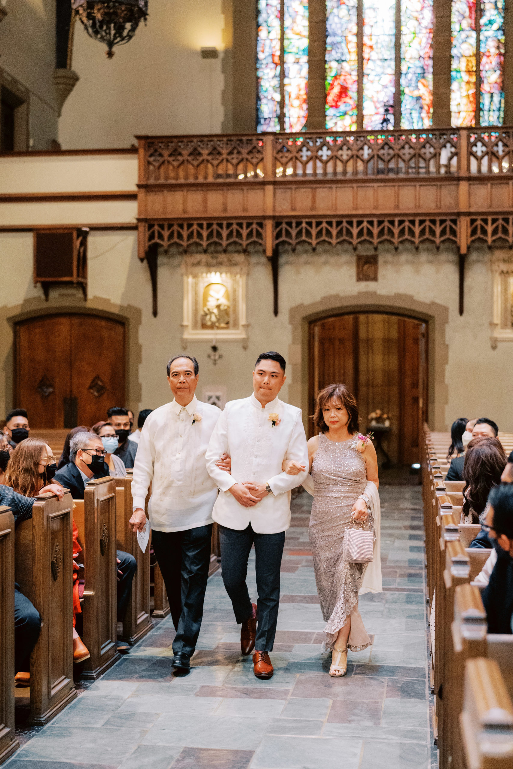 groom with mother and father walk down aisle in church wedding ceremony
