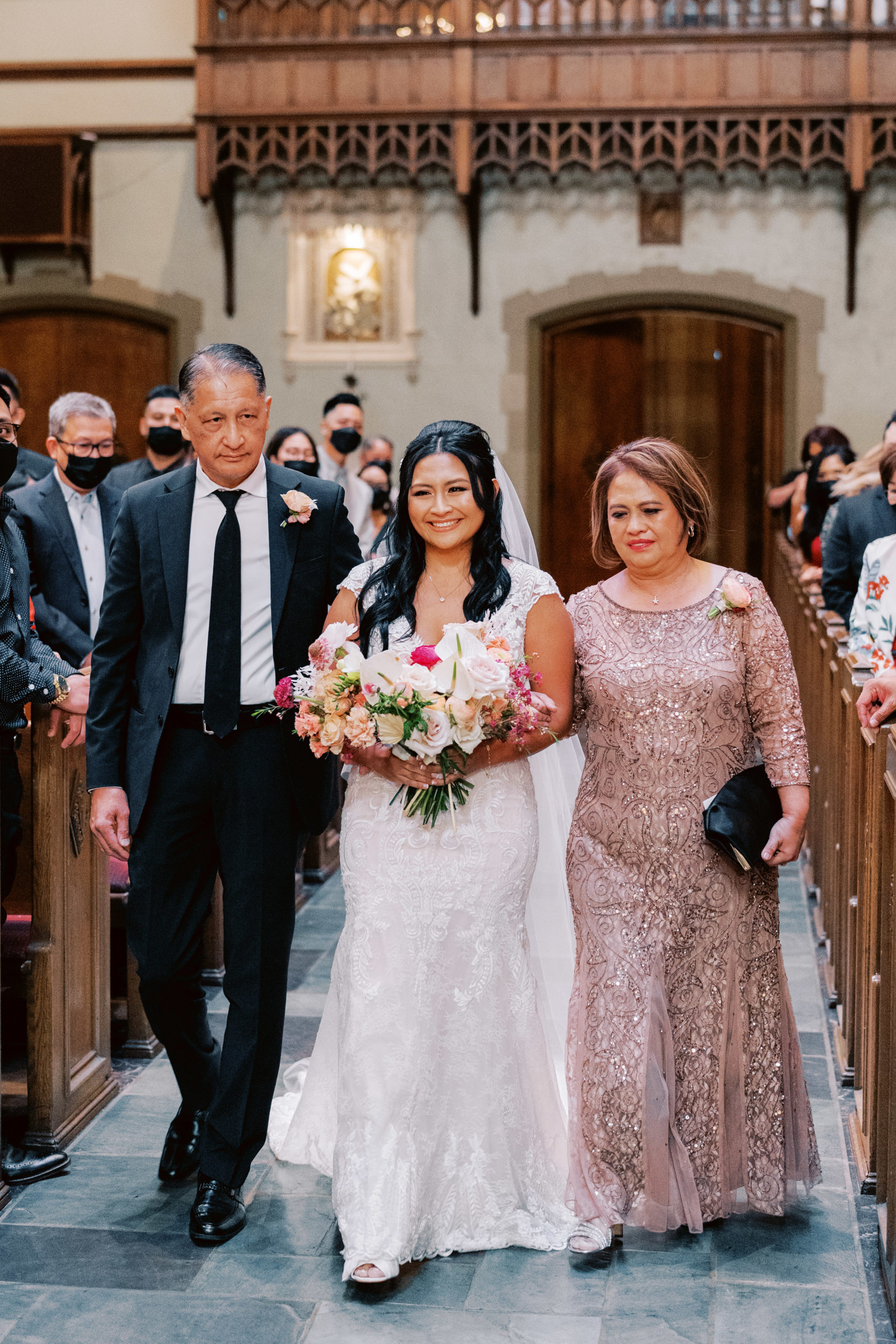 bride with mother and father walks down aisle in church wedding ceremony