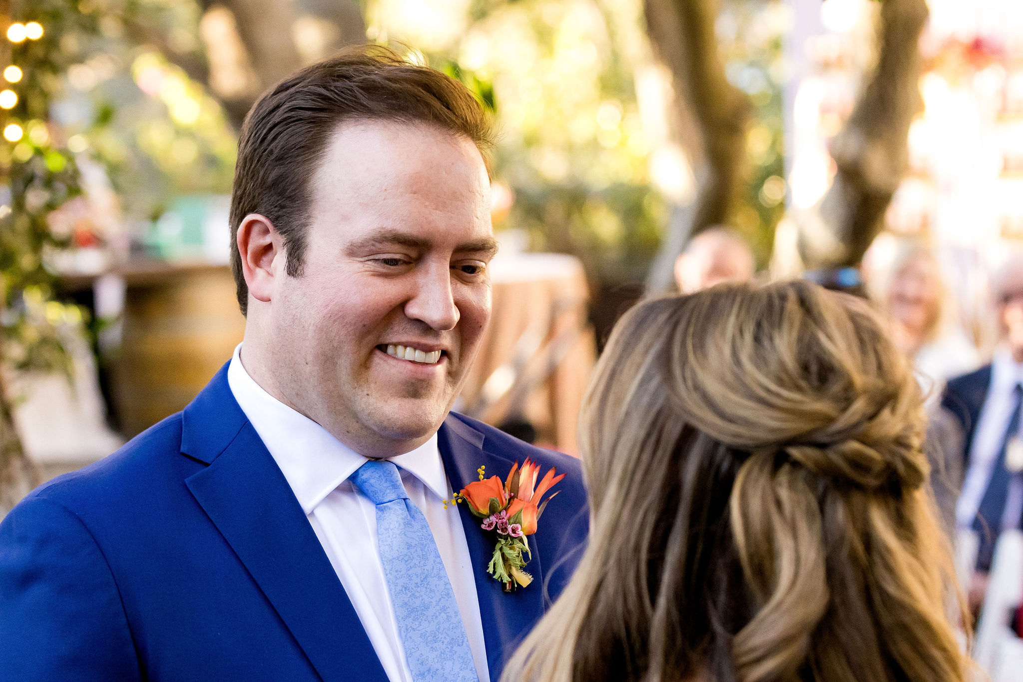 groom in blue suit and tie and bright orange boutonniere smiles at bride during wedding ceremony