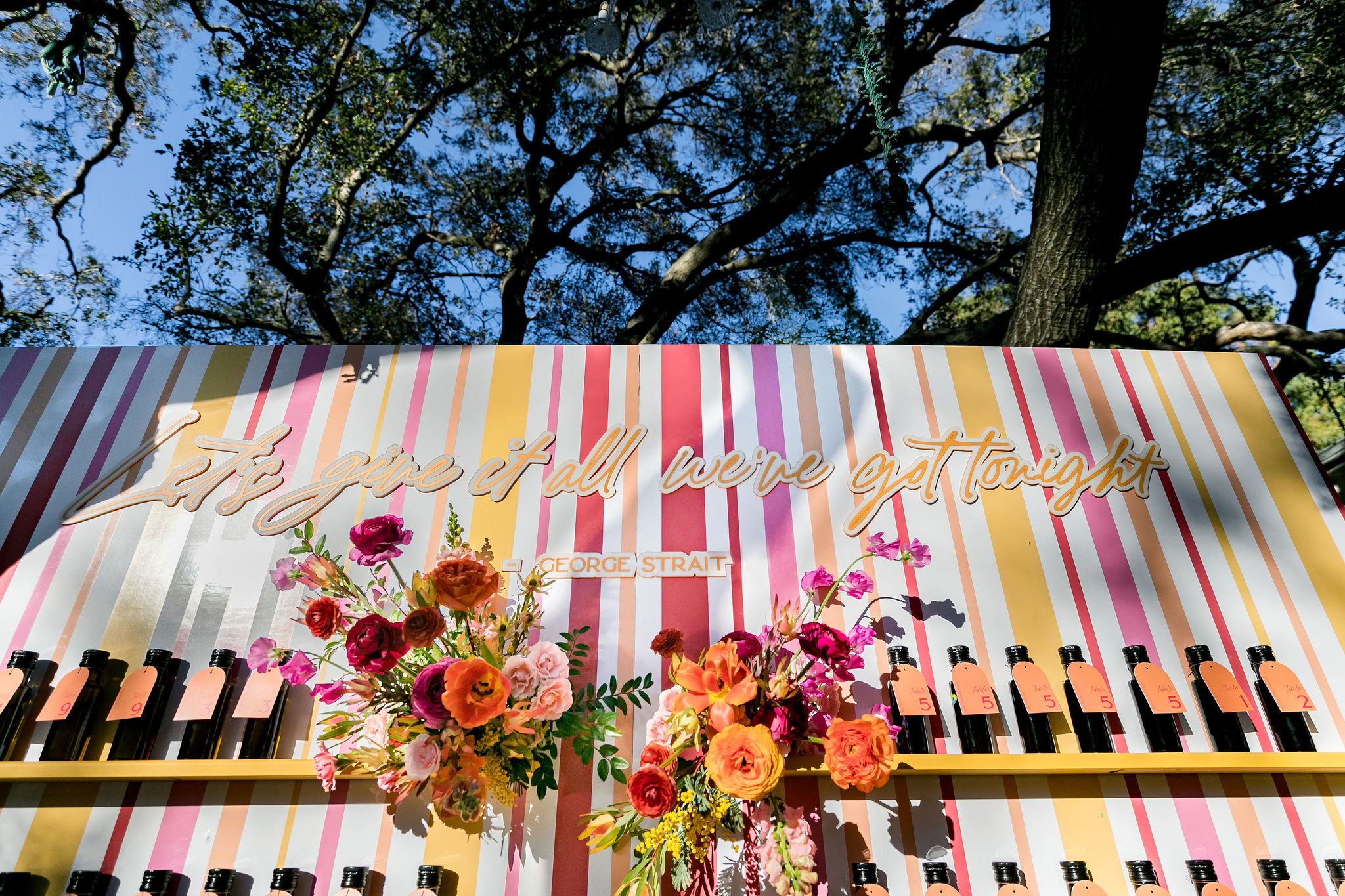 bright pink, orange, yellow and red seating chart display with country music lyrics and individual bottles of olive oil displaying table numbers