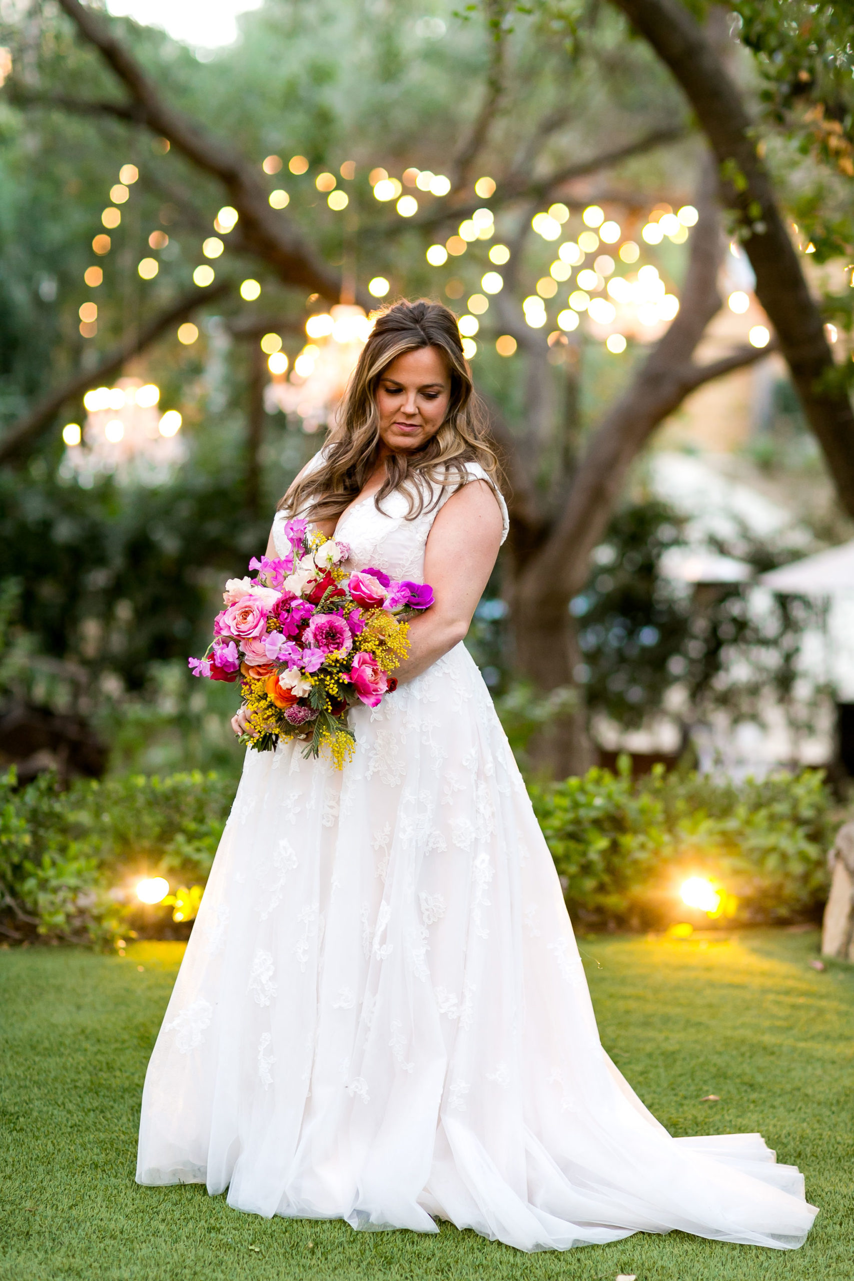 bride in v-neck wedding dress with lace overlay holding a bright purple and pink bouquet