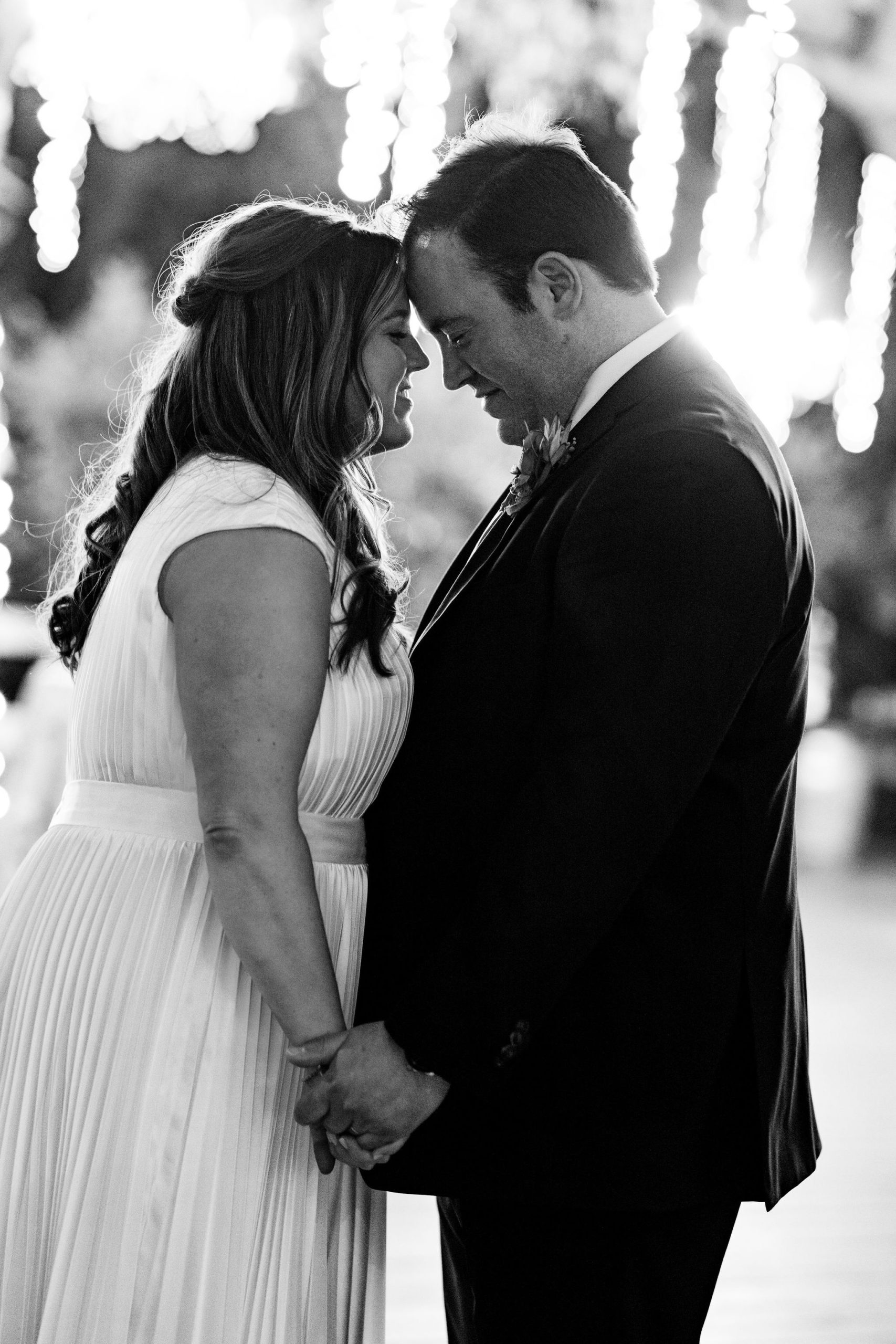 black and white photo of bride and groom with lights blurred in background