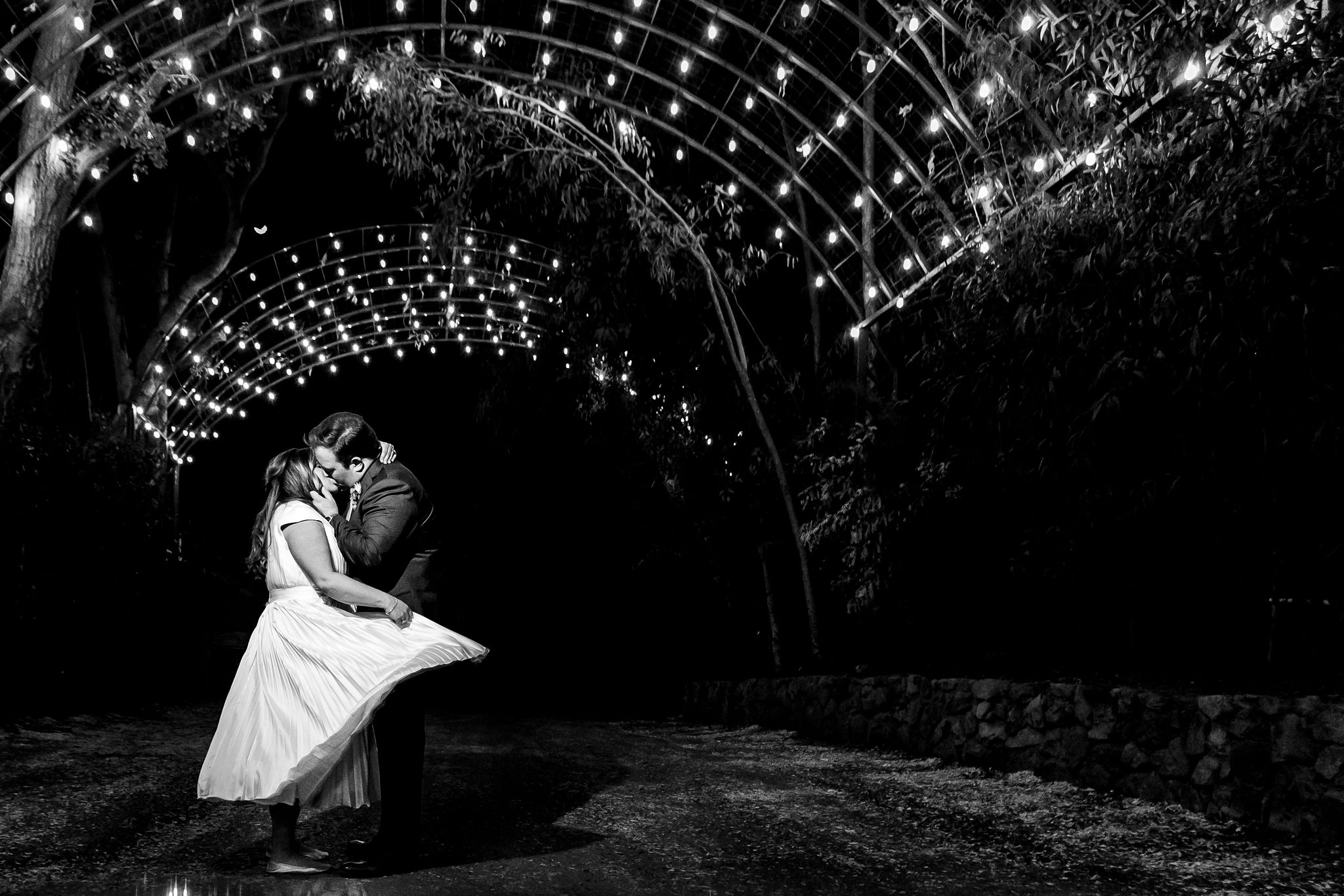 black and white photo of bride and groom under illuminated arch