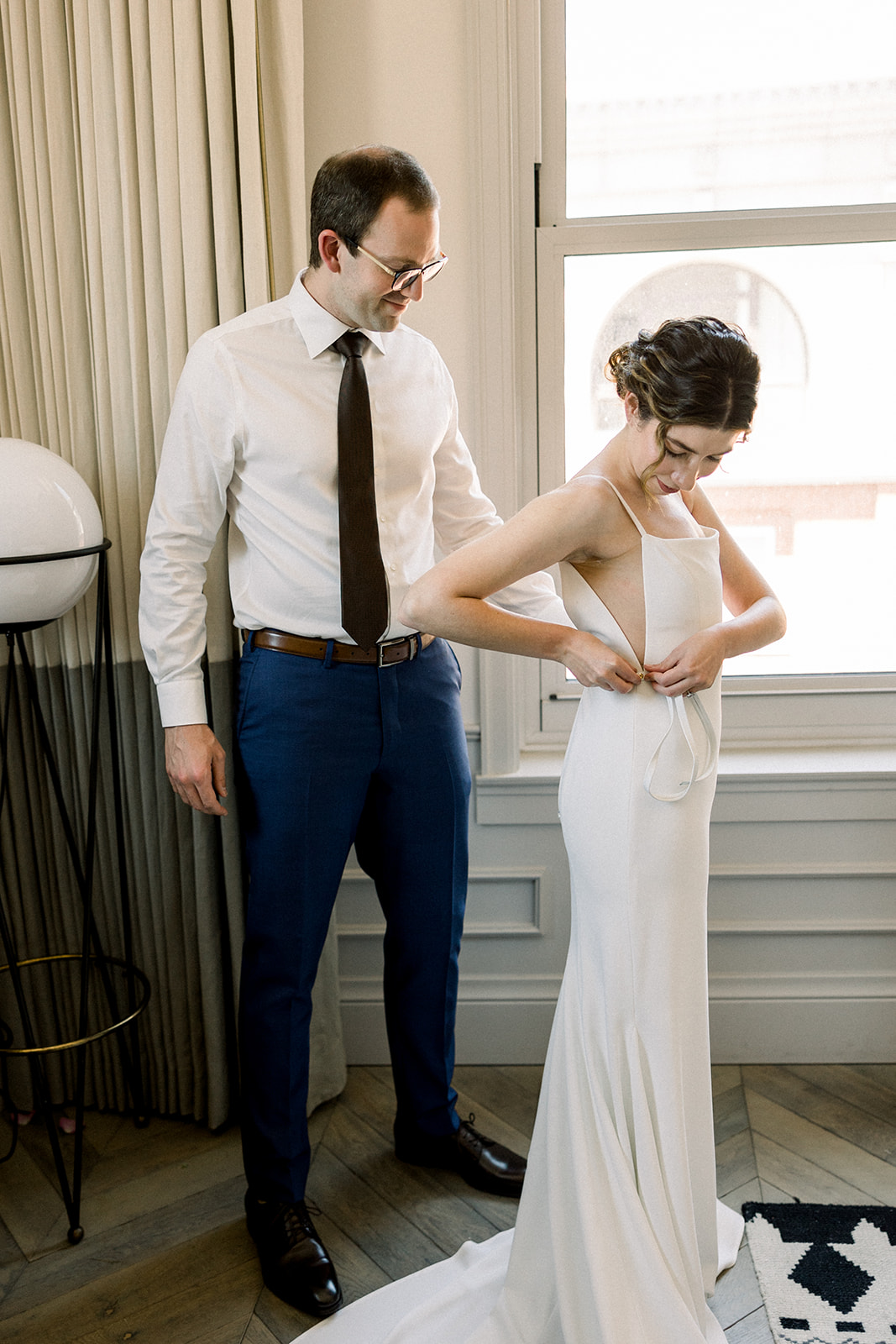 bride in contemporary wedding dress gets ready with groom in white shirt and navy pants 