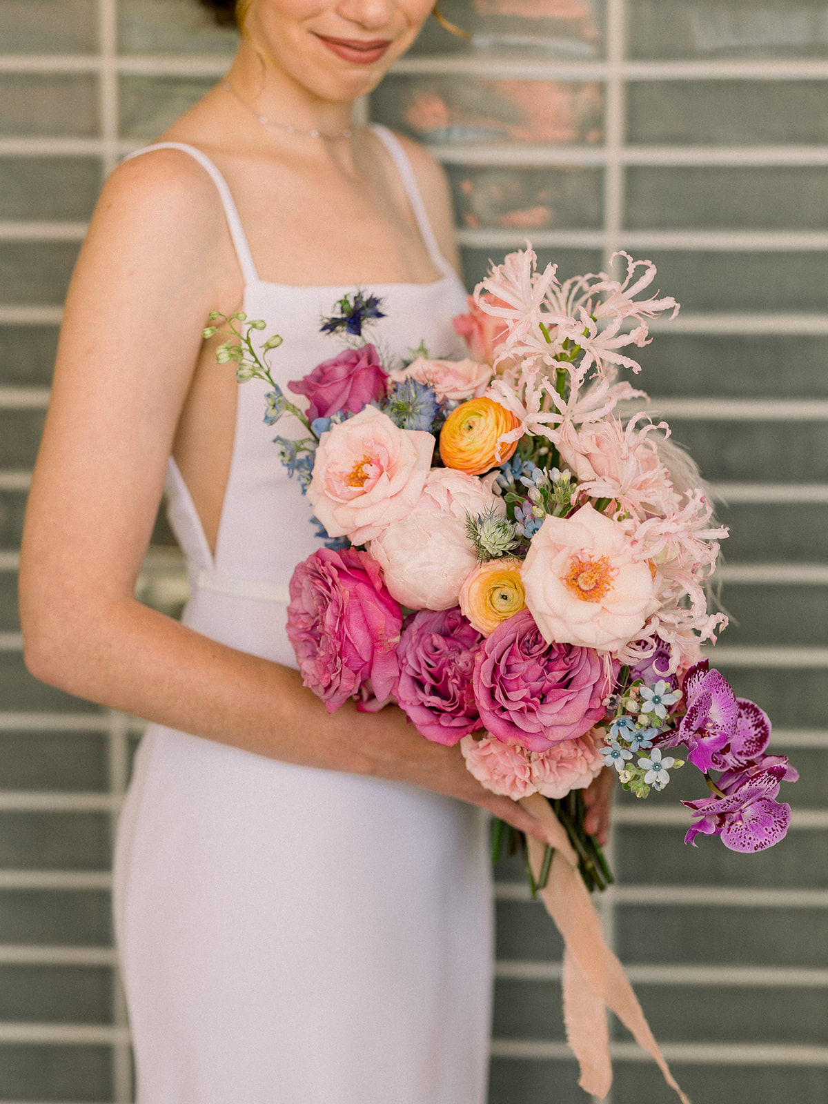 bride in contemporary spaghetti strap dress and low chignon bun with pastel floral bridal bouquet