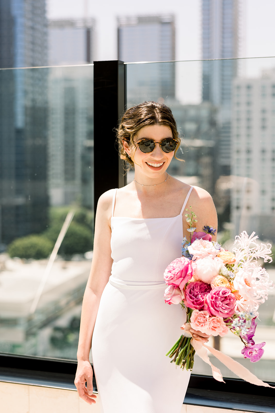 bride in contemporary spaghetti strap dress stands on rooftop with DTLA skyline in background