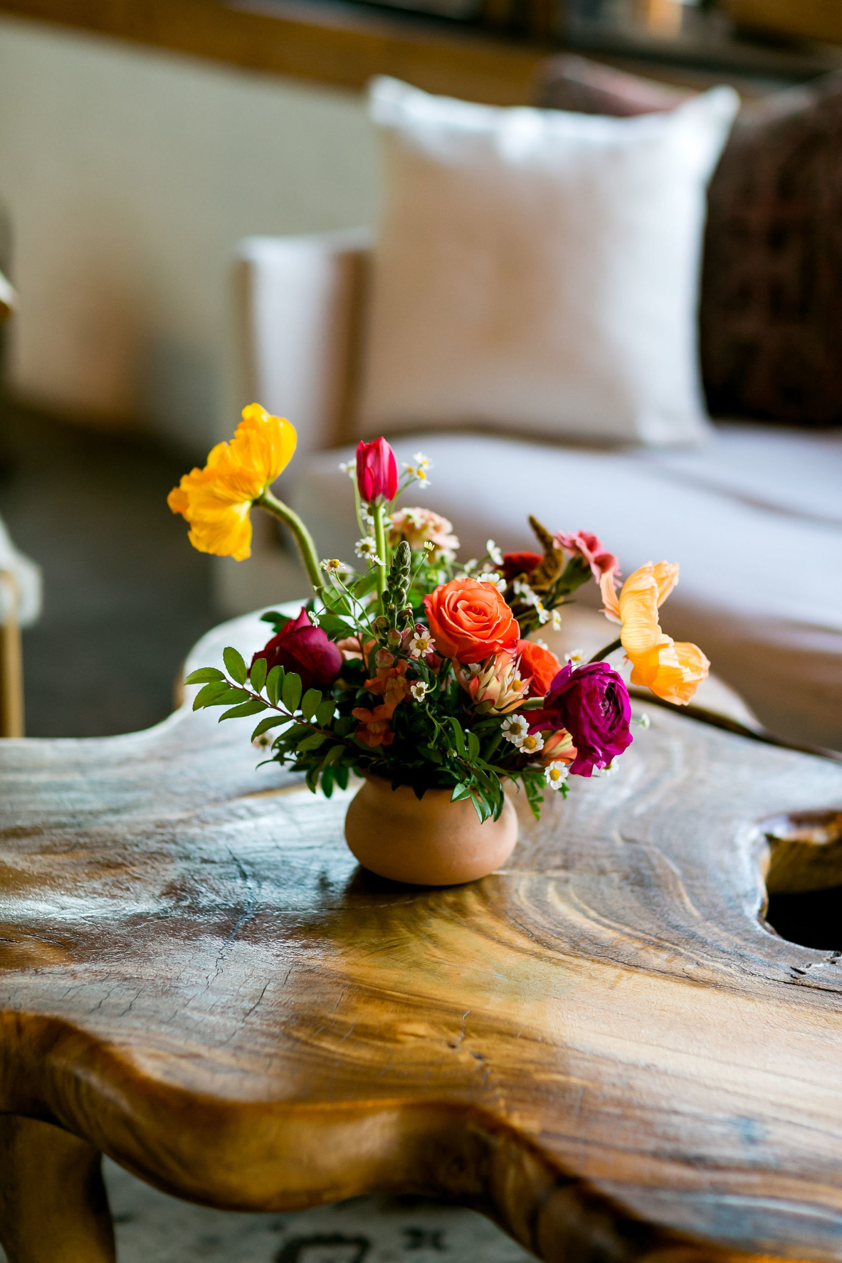 bright floral centerpiece in terra-cotta  pot on raw wooden coffee table