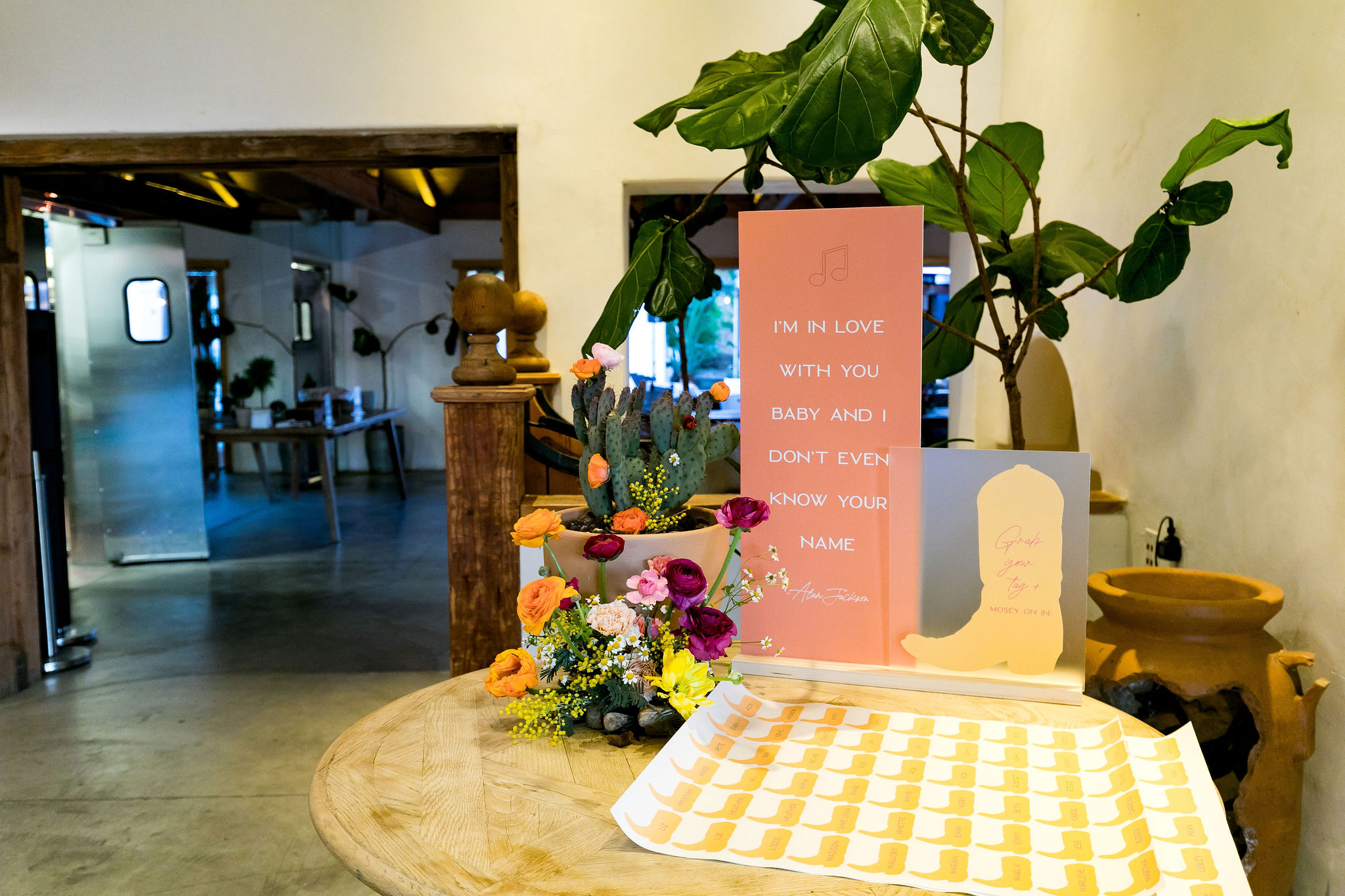 country themed wedding welcome party with welcome table featuring sign with Alan Jackson lyrics and cowboy boot name tags