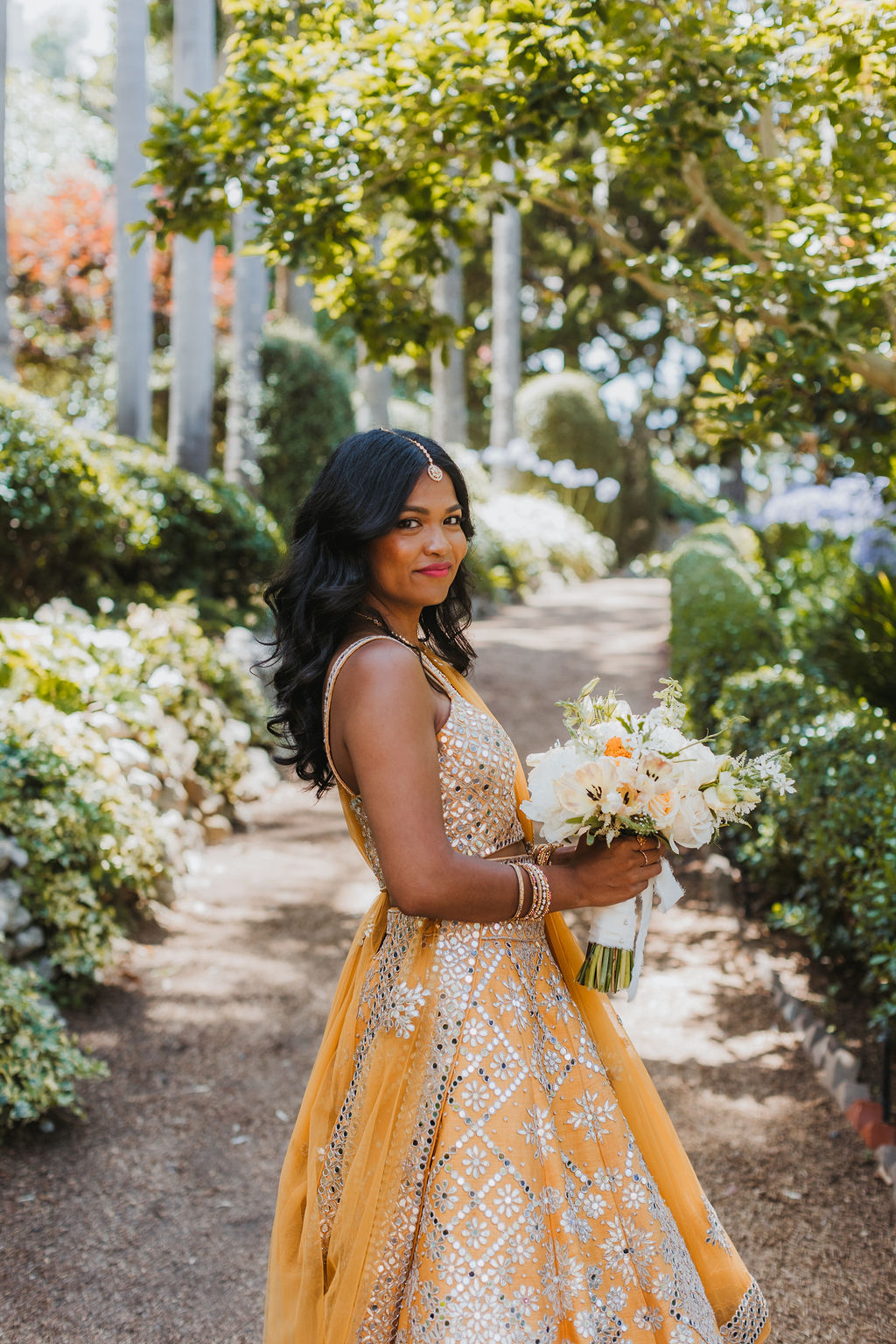 bride in orange marigold colored wedding sari holds bouquet of white and orange flowers during portraits 