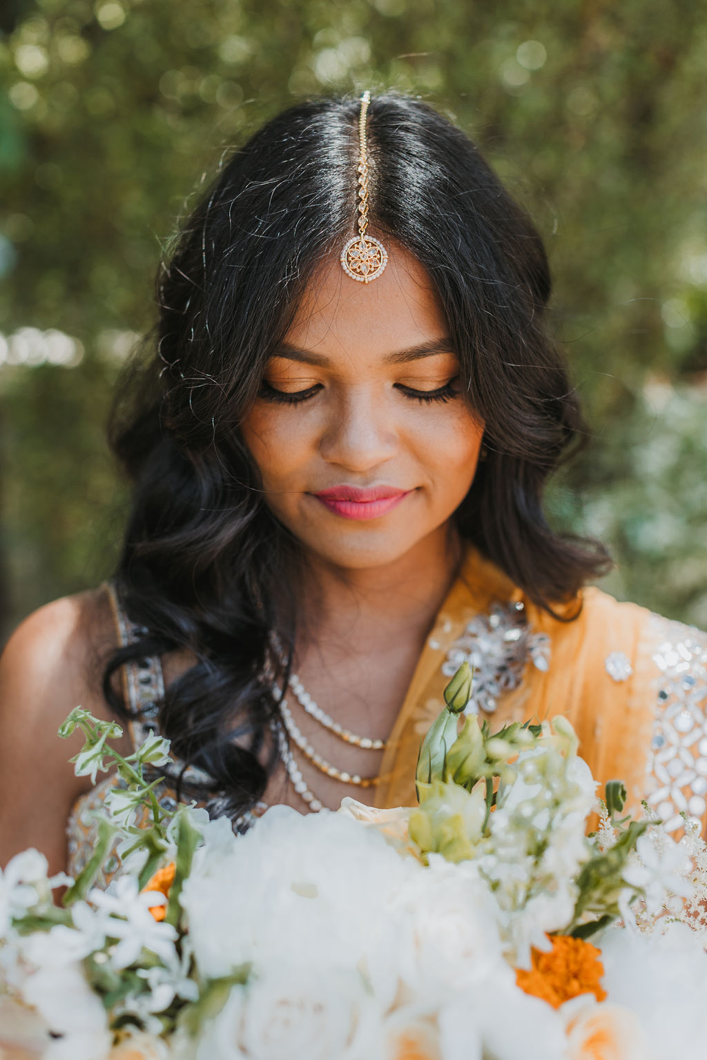 bride in orange marigold colored wedding sari holds bouquet of white and orange flowers 