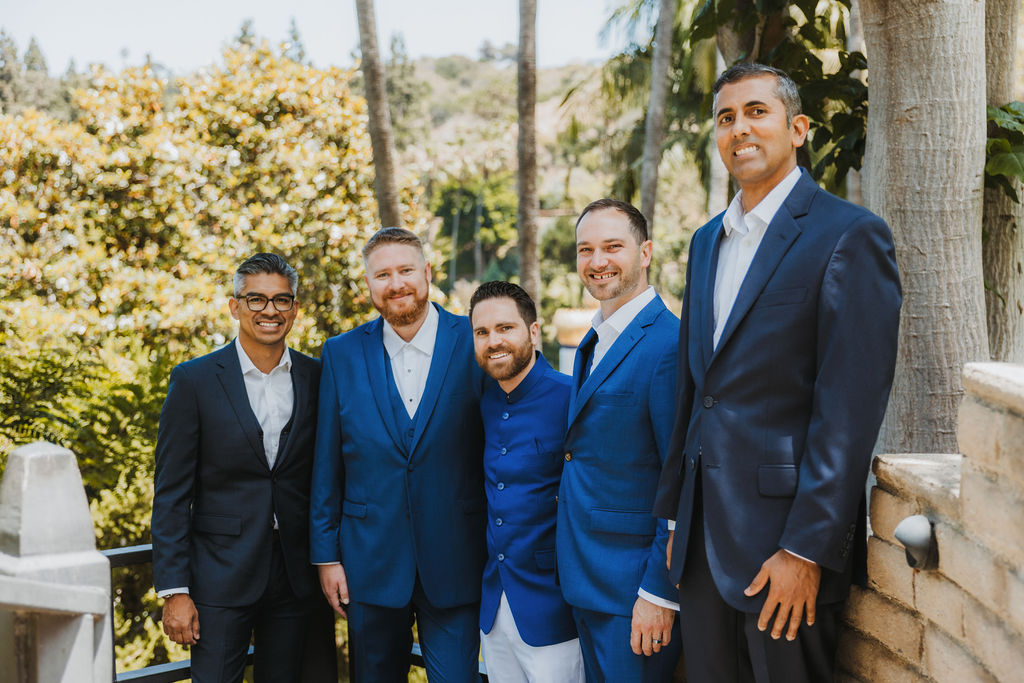 groom with beard wearing cobalt blue suit stands with groomsmen in blue and grey suits