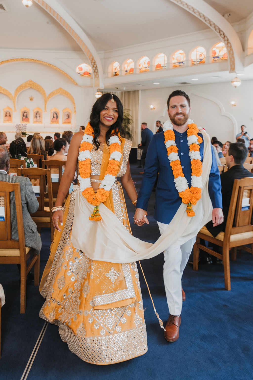 bride and groom recessional during Hindu and Christian wedding ceremony at Lake Shrine Temple in Malibu with orange color palette