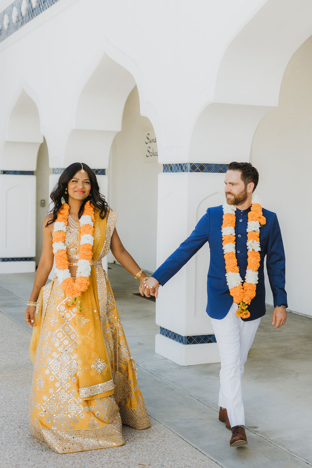 bride in orange sari with groom in cobalt blue suit wearing marigold garland take portrait photos at Lake Shrine Temple in Malibu