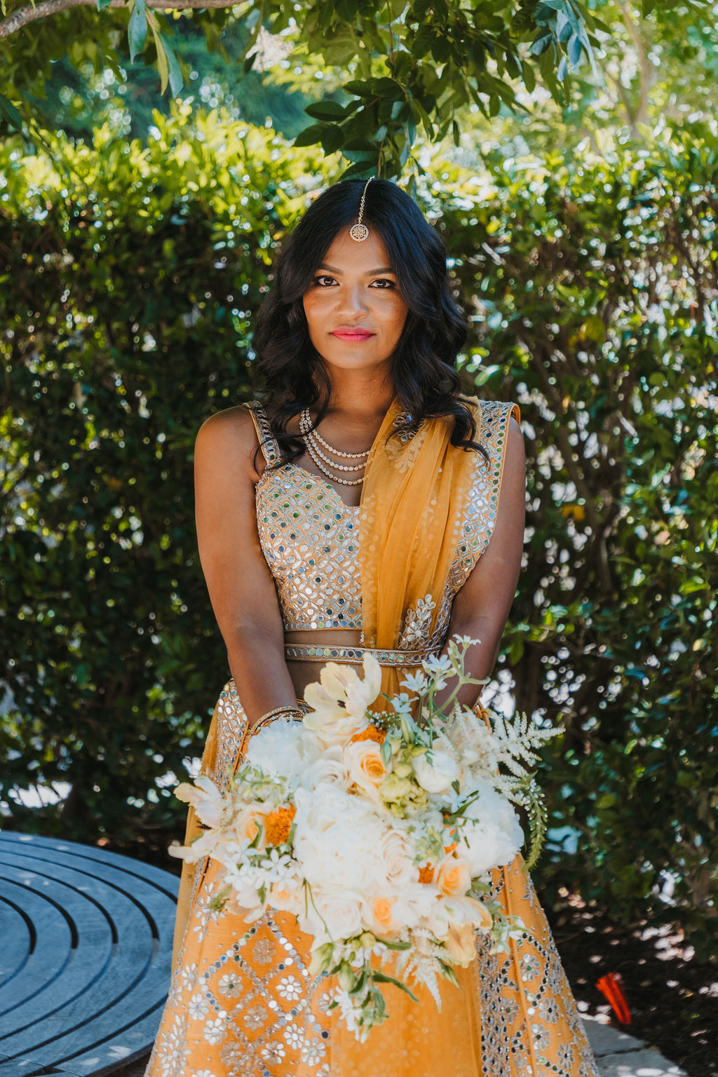 bride in orange marigold colored wedding sari holds bouquet of white and orange flowers