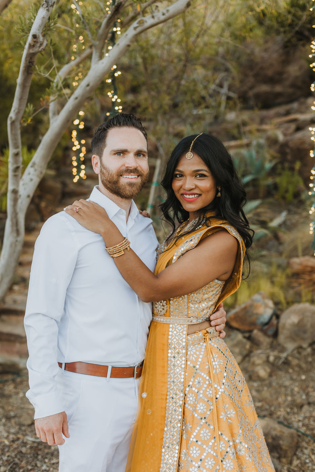 bride in orange sari stands with groom in white during sunset photos at Saddlerock Ranch in Malibu
