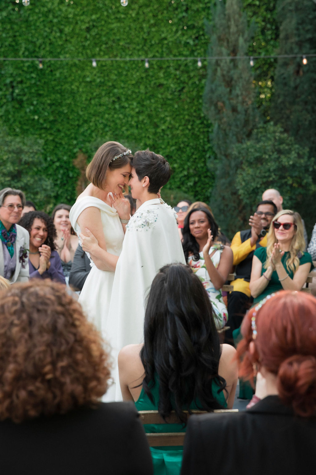 two brides wearing coordinating bridal attire share first kiss during outdoor wedding ceremony at the Fig House