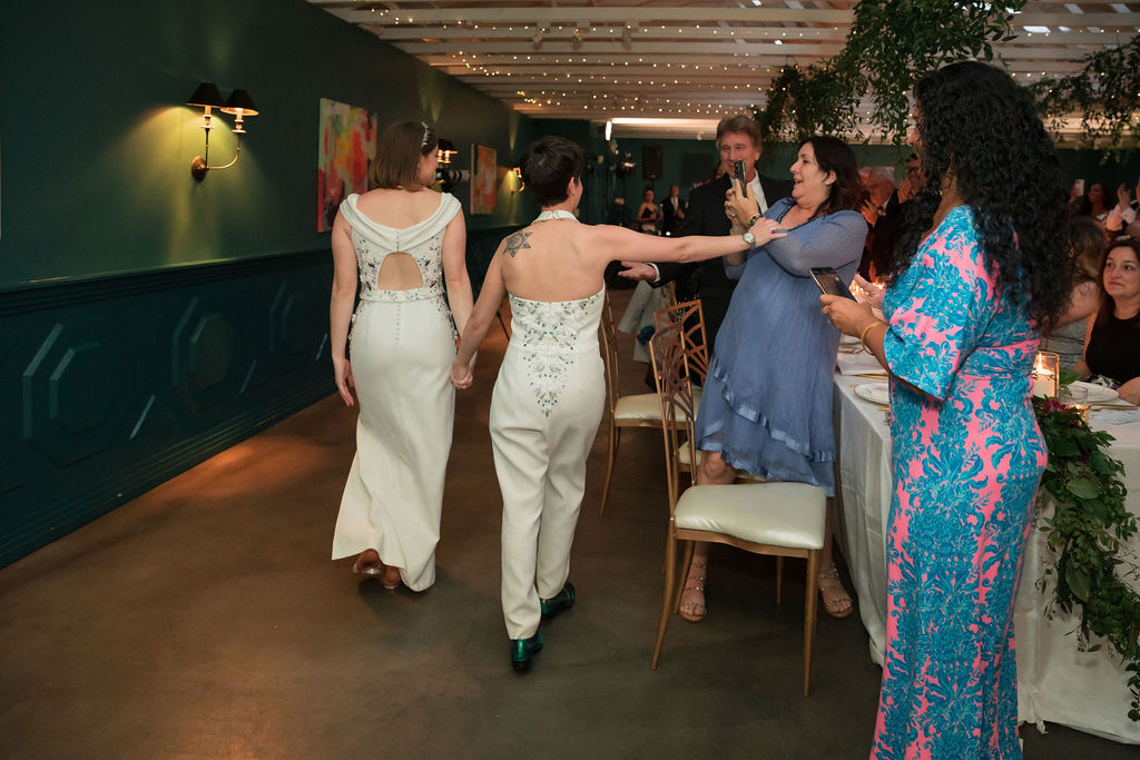 brides in coordinating embeliished bridal dress and bridal jumpsuit hold hands during grand entrance of wedding reception at The Fig House
